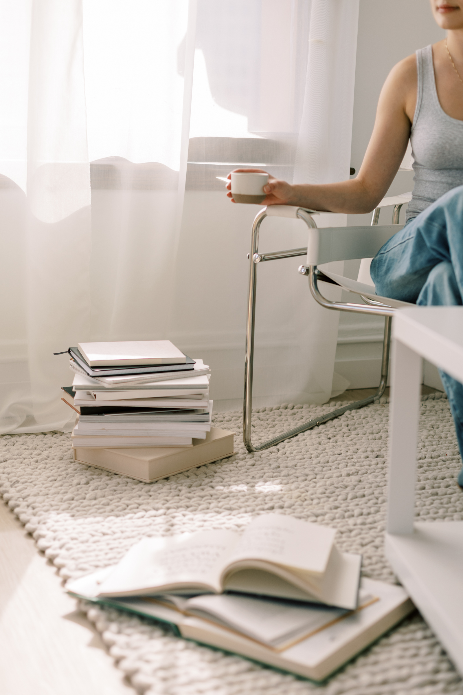 Pile of books on the floor and a woman sitting at a desk with a cup of coffee in hand